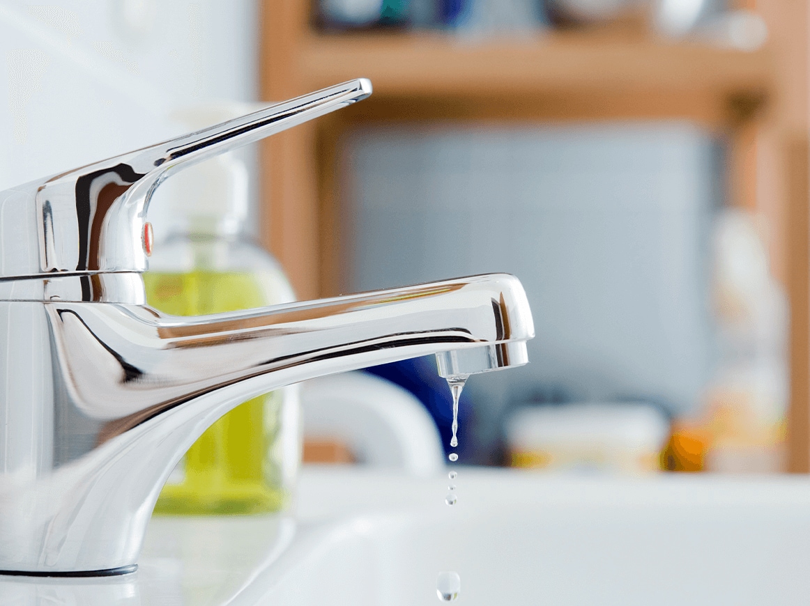 Dripping sink faucet with cleaning supplies in the background